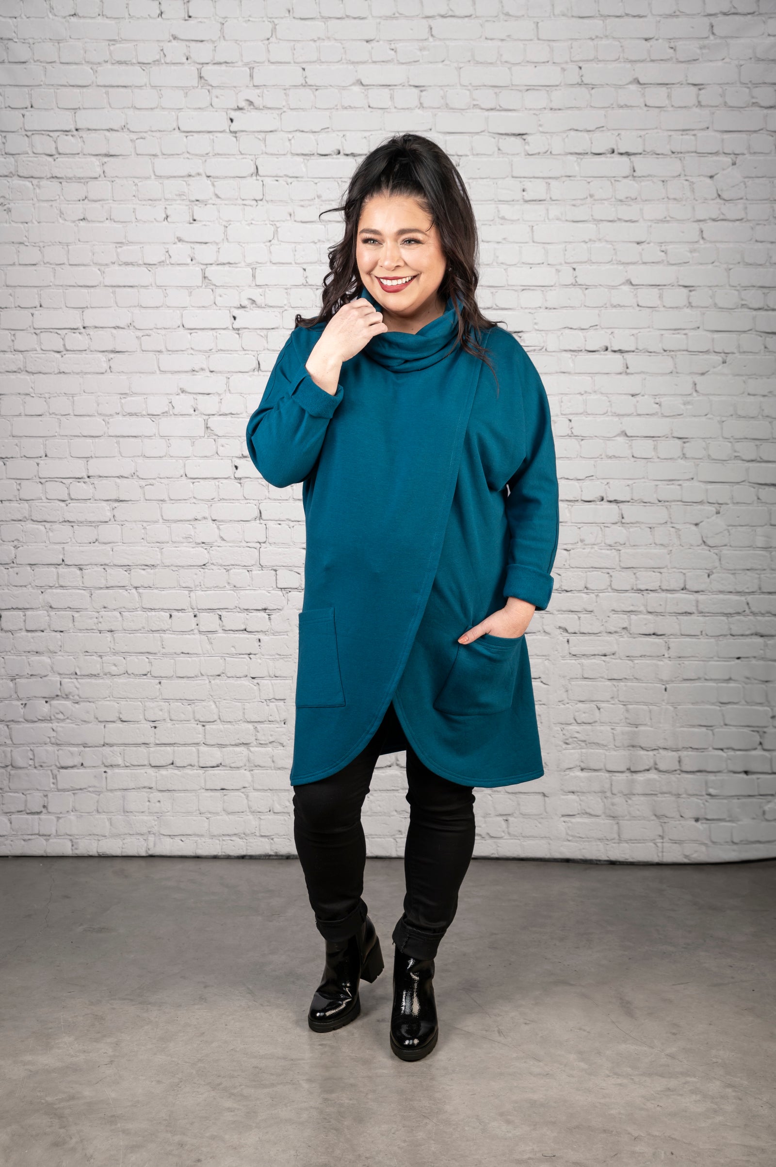 Woman wearing a teal coat against a white brick wall.