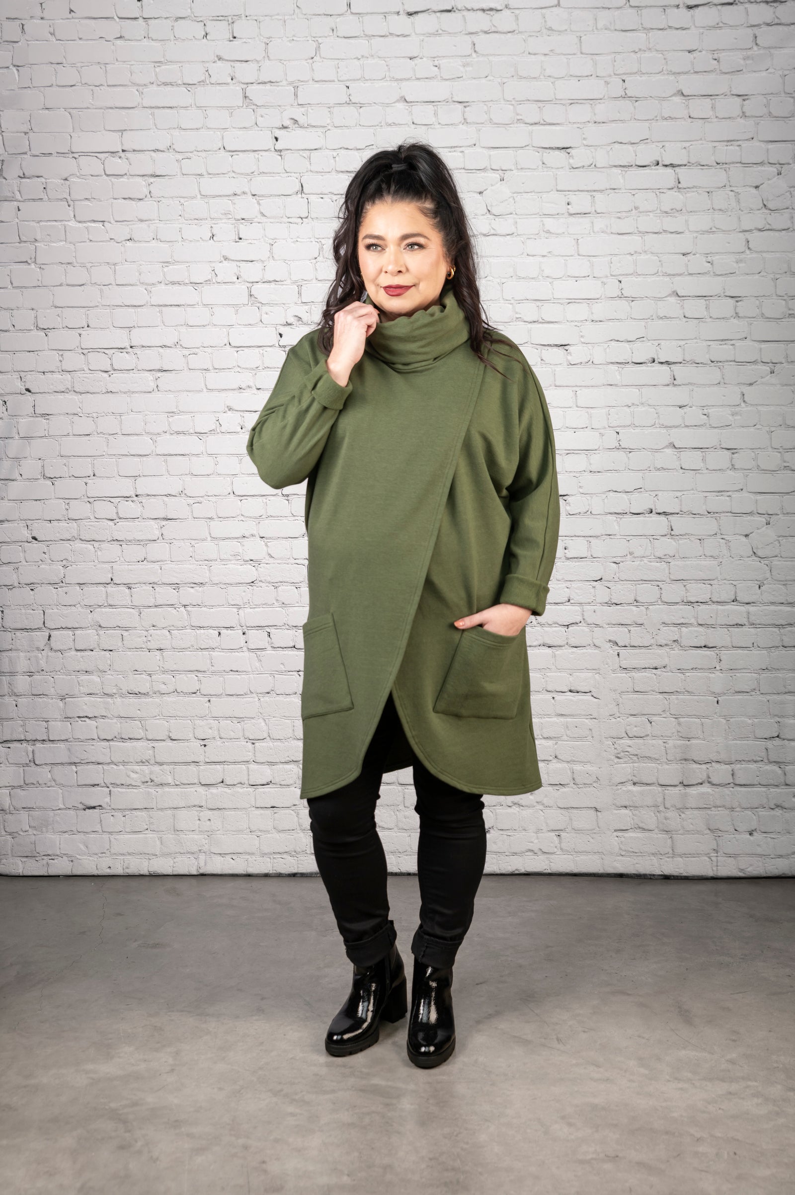 Woman wearing a teal coat against a white brick wall.